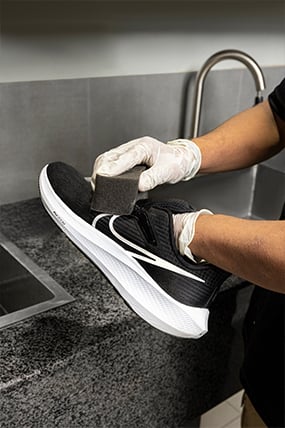 Worker cleaning a black sneaker with a sponge at Jab Chaho